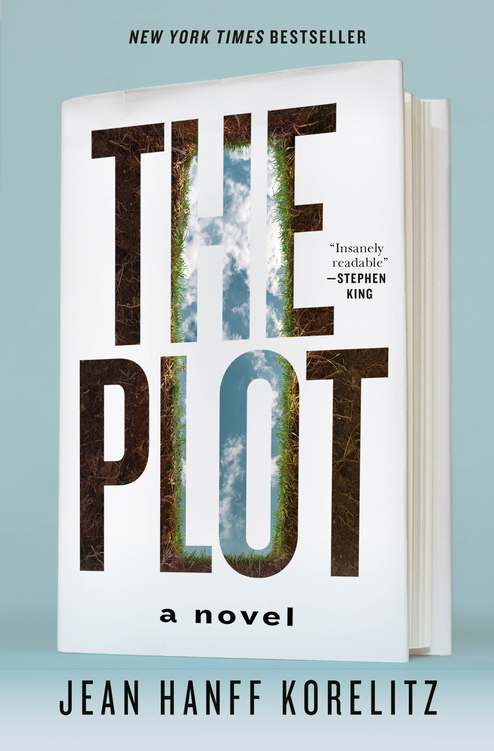 Book cover of The Plot by Jean Hanff Korelitz featuring a white book against a pale blue background, with the title cut into the cover to reveal an image of earth and sky beneath. The design creates the illusion of a deep trench or opening, emphasizing the novel's mystery theme.