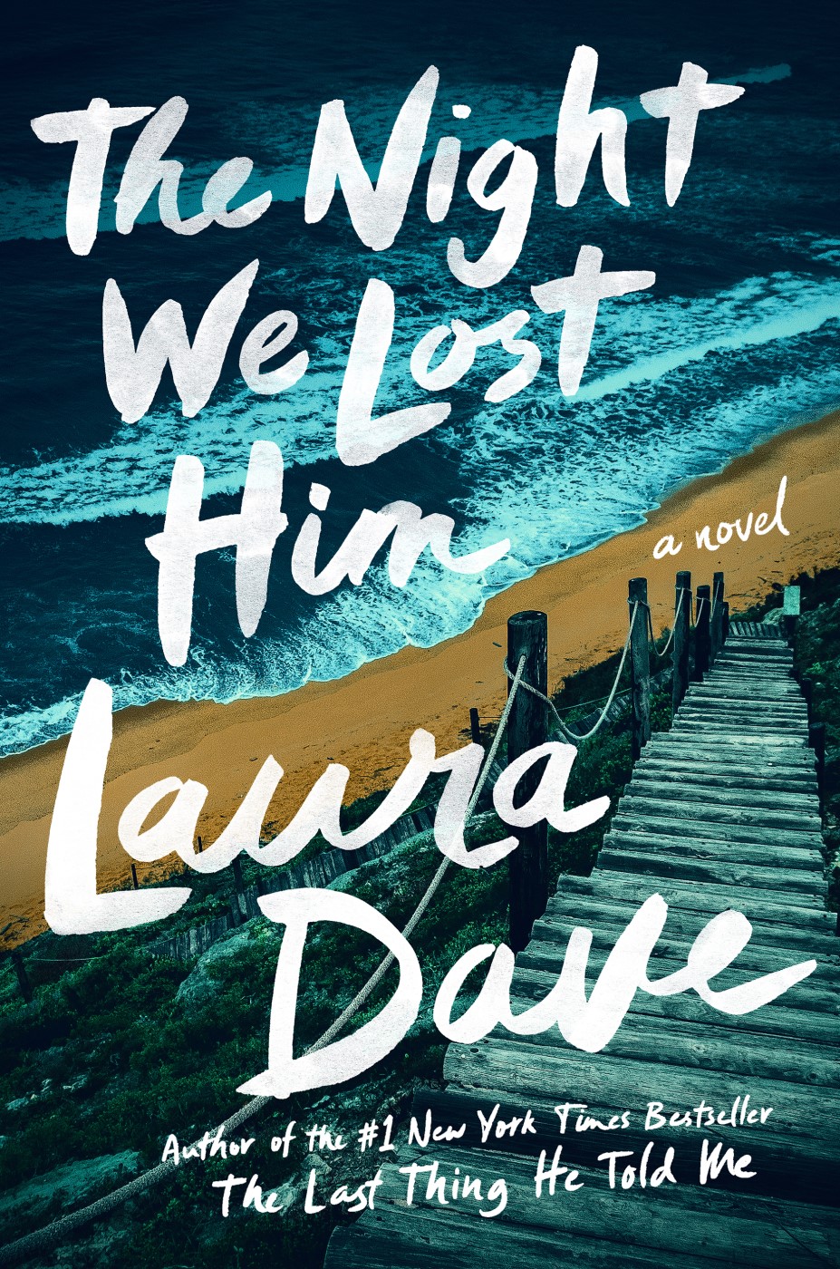 Book cover of The Night We Lost Him by Laura Dave featuring an aerial view of ocean waves along a sandy beach, a wooden stairway descending toward the shore, and large handwritten-style white title text. The image uses deep blue and teal tones to create a moody coastal atmosphere.