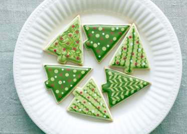Six Christmas tree-shaped cookies decorated with green and white icing arranged on a white plate.
