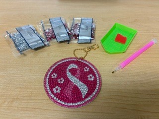 Pink ribbon diamond art keychain with crafting beads, tray, and stylus laid out on a table.