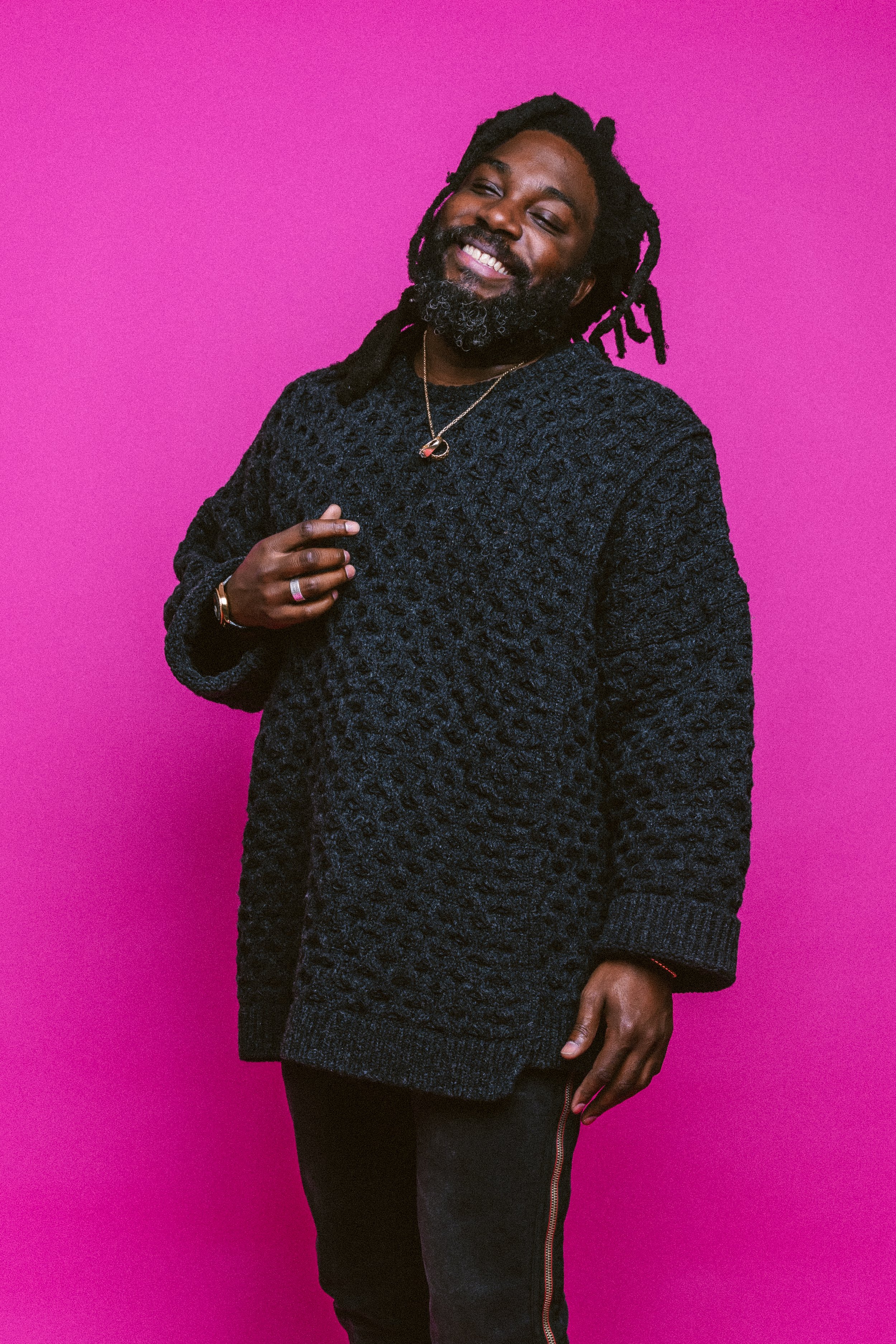Jason Reynolds, laughing, standing with a pink background behind him