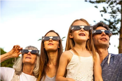 Four family members wearing solar eclipse glasses looking toward the sky