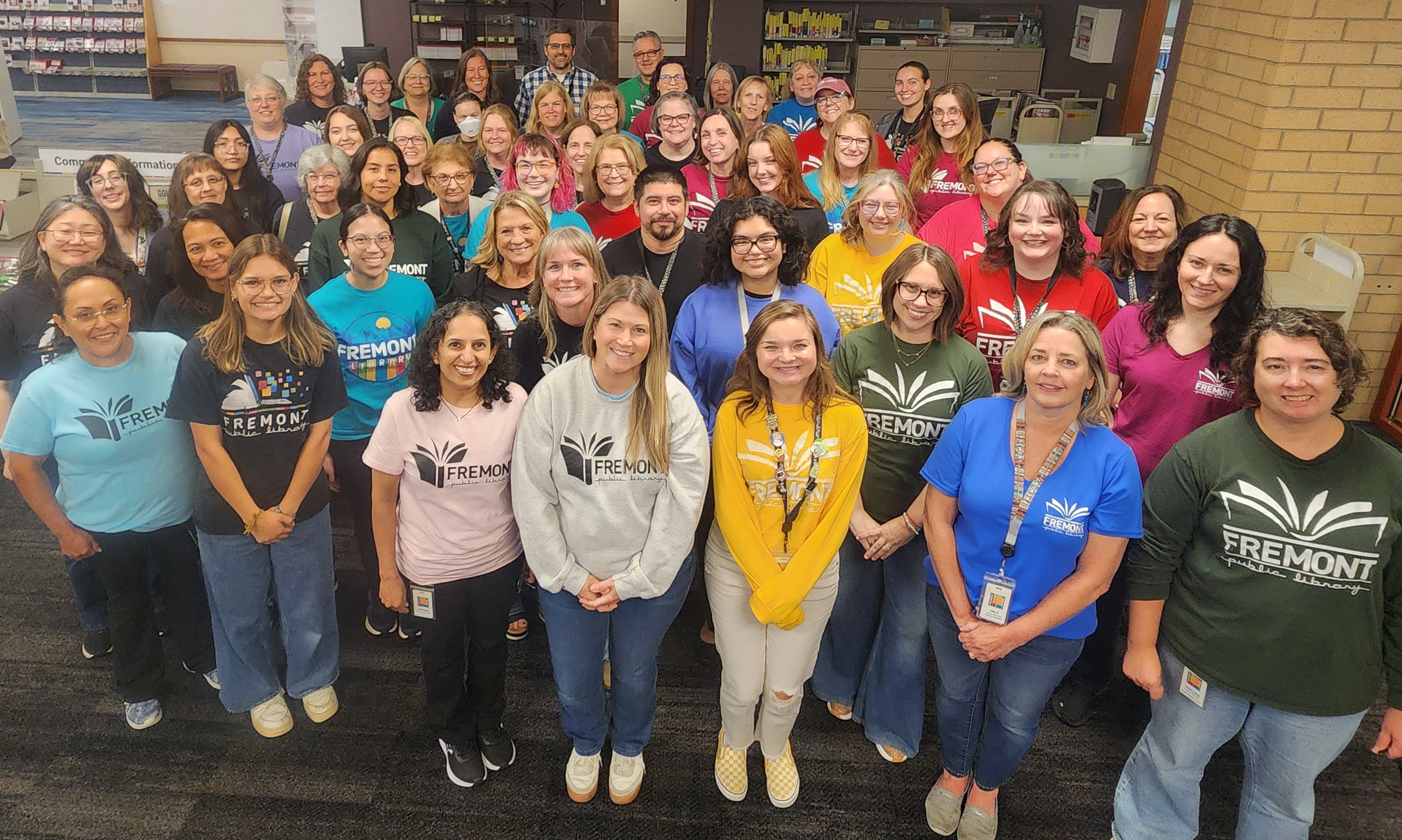 picture of about 52 staff members in front of the library's Checkout Desk  wearing various Fremont t-shirts