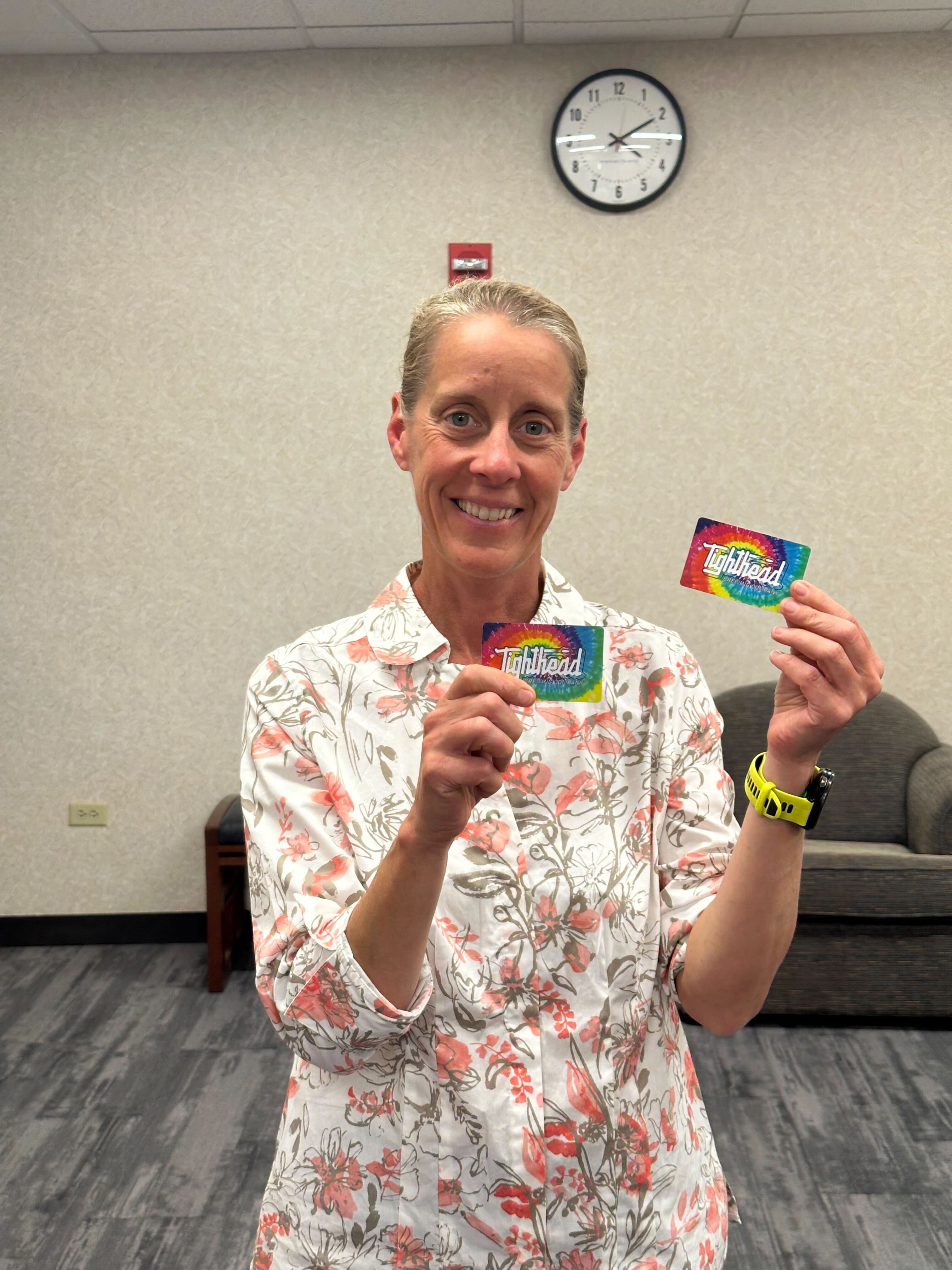woman with short blond hair holding up the two gift cards to Tighthead Brewery