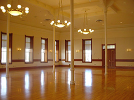 A large empty ballroom with four central pillars and three chandeliers
