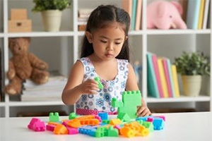 A young girl stacking large lego blocks from a discovery kit on a table