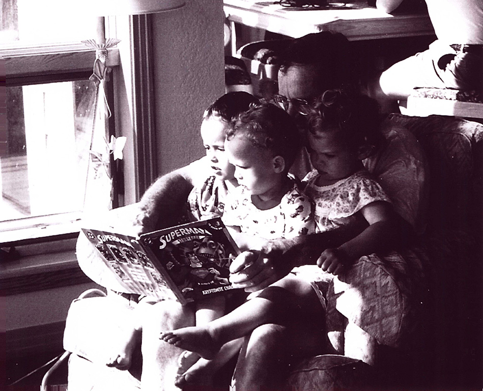 Father reading a story to the three toddlers sitting on his laps