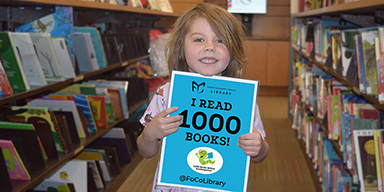 Little girl holding the 1000 books milestone sign inside the library