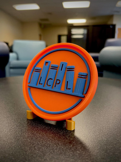3D printed orange medallion with a blue LCPL logo raised in the center