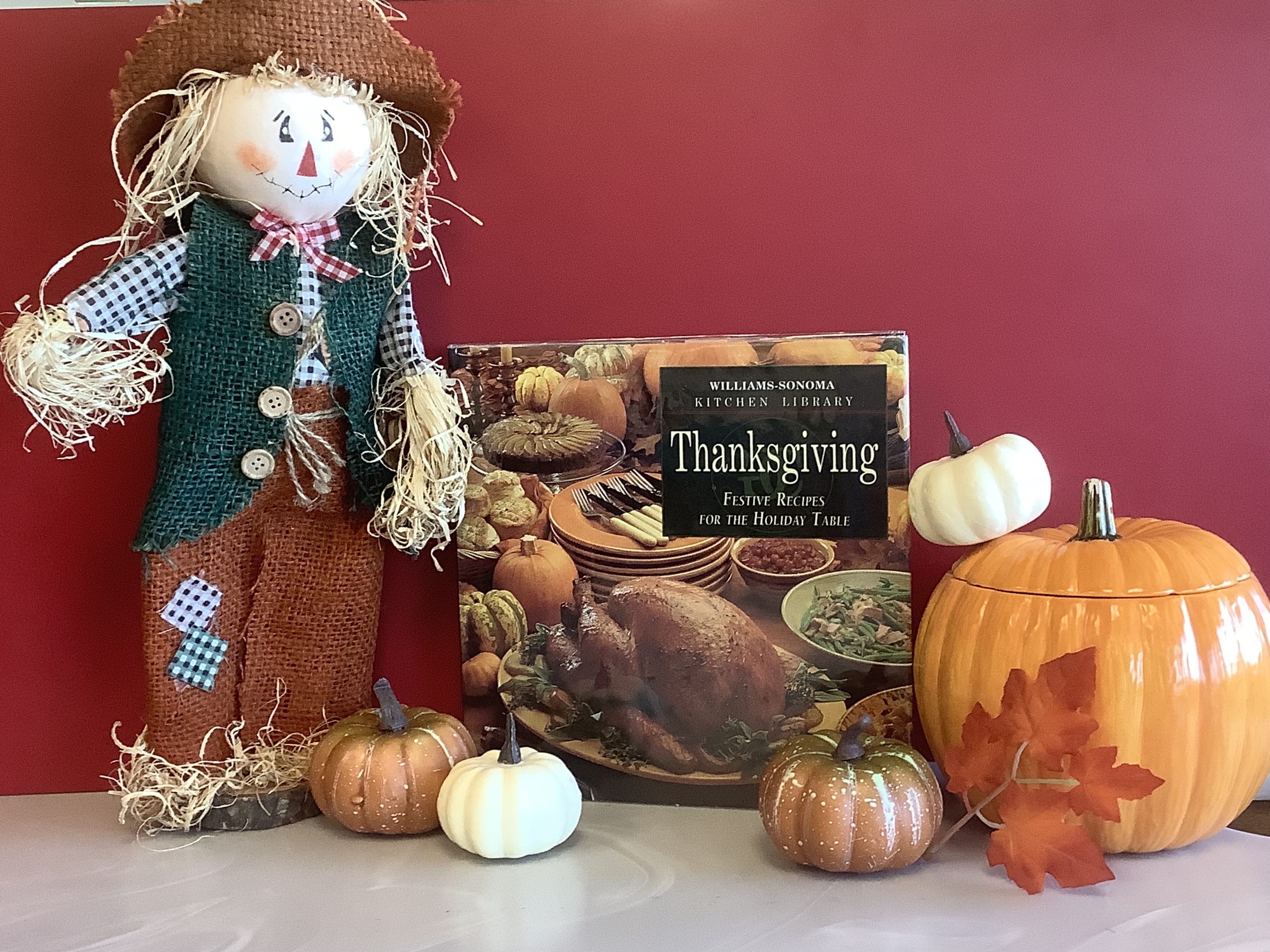 A scarecrow and some decorative pumpkins surrounding the Williams Sonoma Kitchen Library Book for Thanksgiving