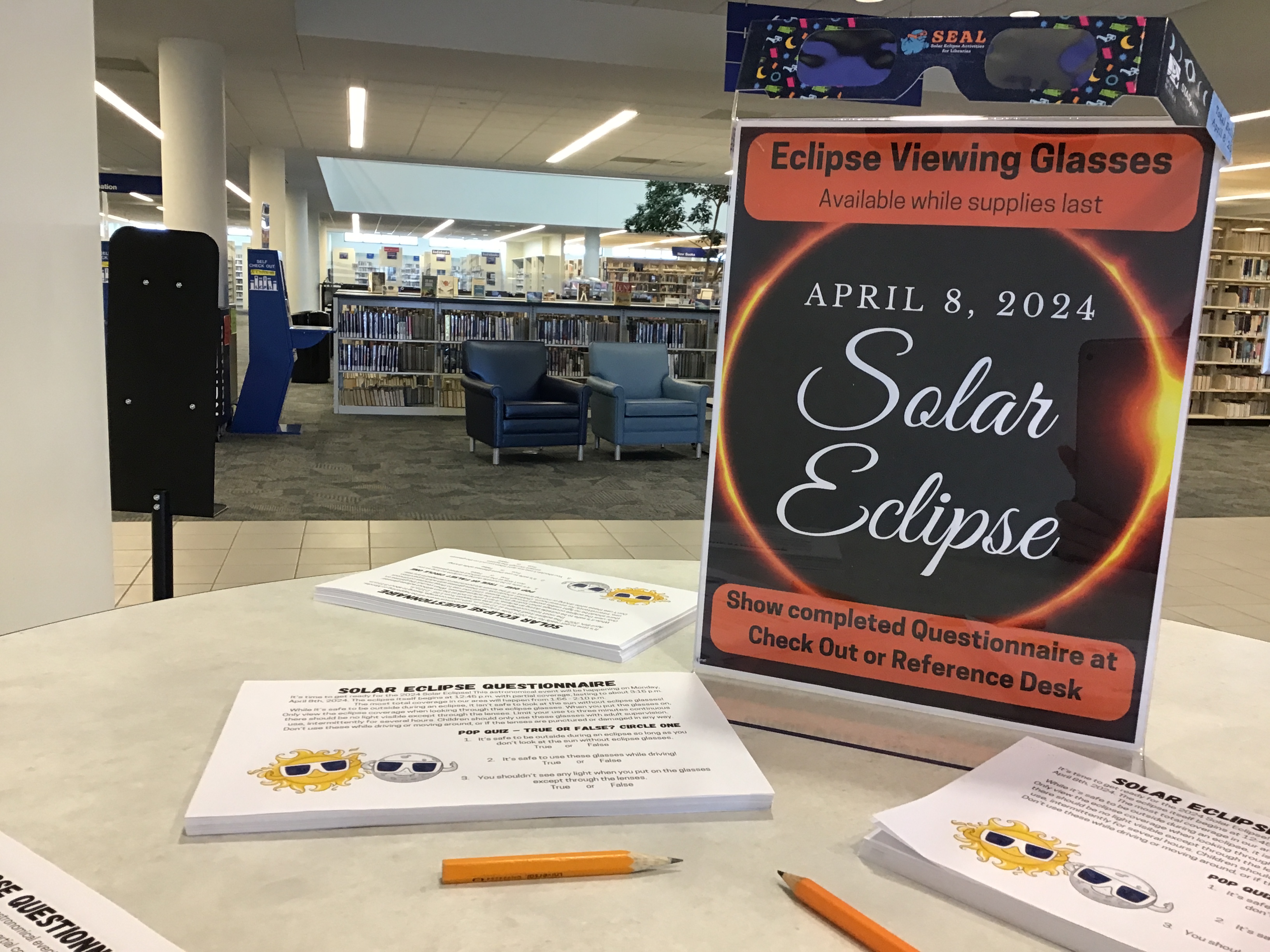 Eclipse glasses atop a sign reading Solar Eclipse. Show completed questionnaire at desk