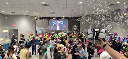 Bubbles explode over top of a crowded library dance floor while Heads, Shoulders, Knees and Toes plays on the projector