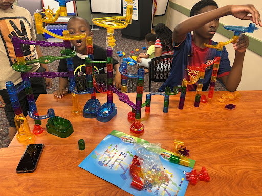 Two tween boys work on building a multicolored plastic marble run on a library table