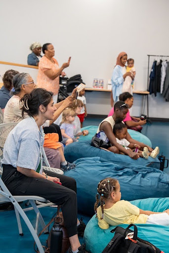 Caregivers and preschoolers on chairs and big blue bean bags watch a play.